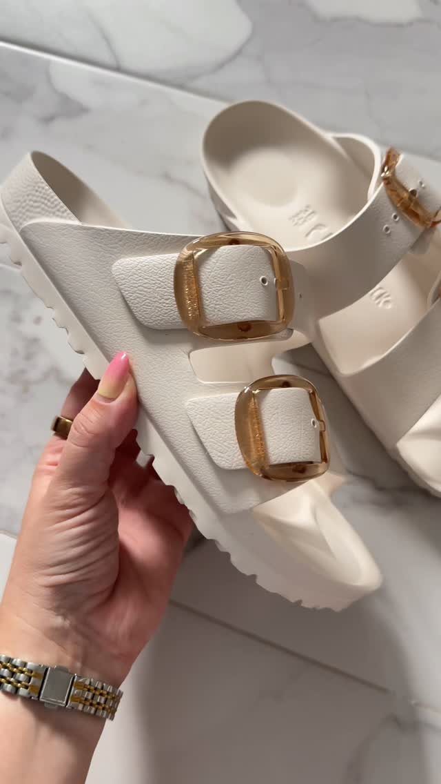 Casual Summer Outfits: 10 Easy Ideas for Daily Wear 10 Cream-colored slide sandals with large amber buckles held by a hand over marble.