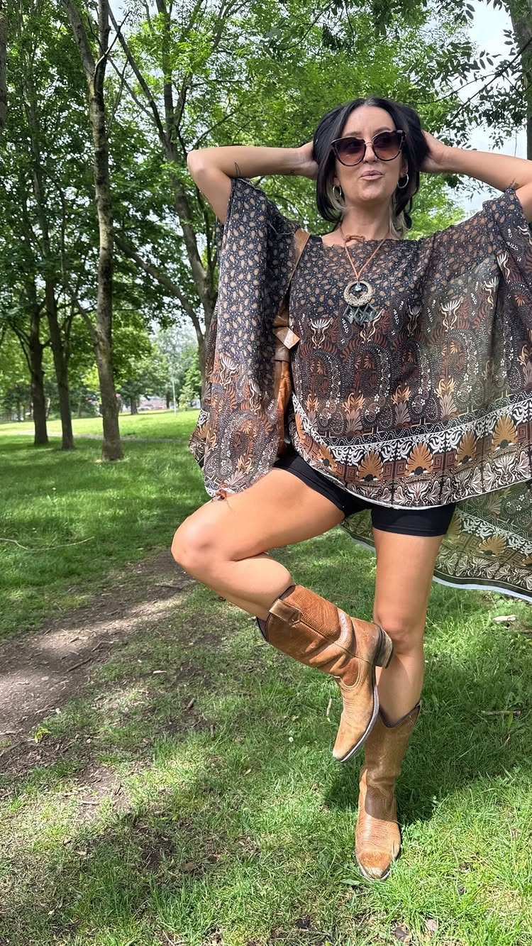 Casual Summer Outfits: 10 Easy Ideas for Daily Wear 6 Woman posing in a park wearing a patterned bohemian poncho, black shorts, and brown cowboy boots.