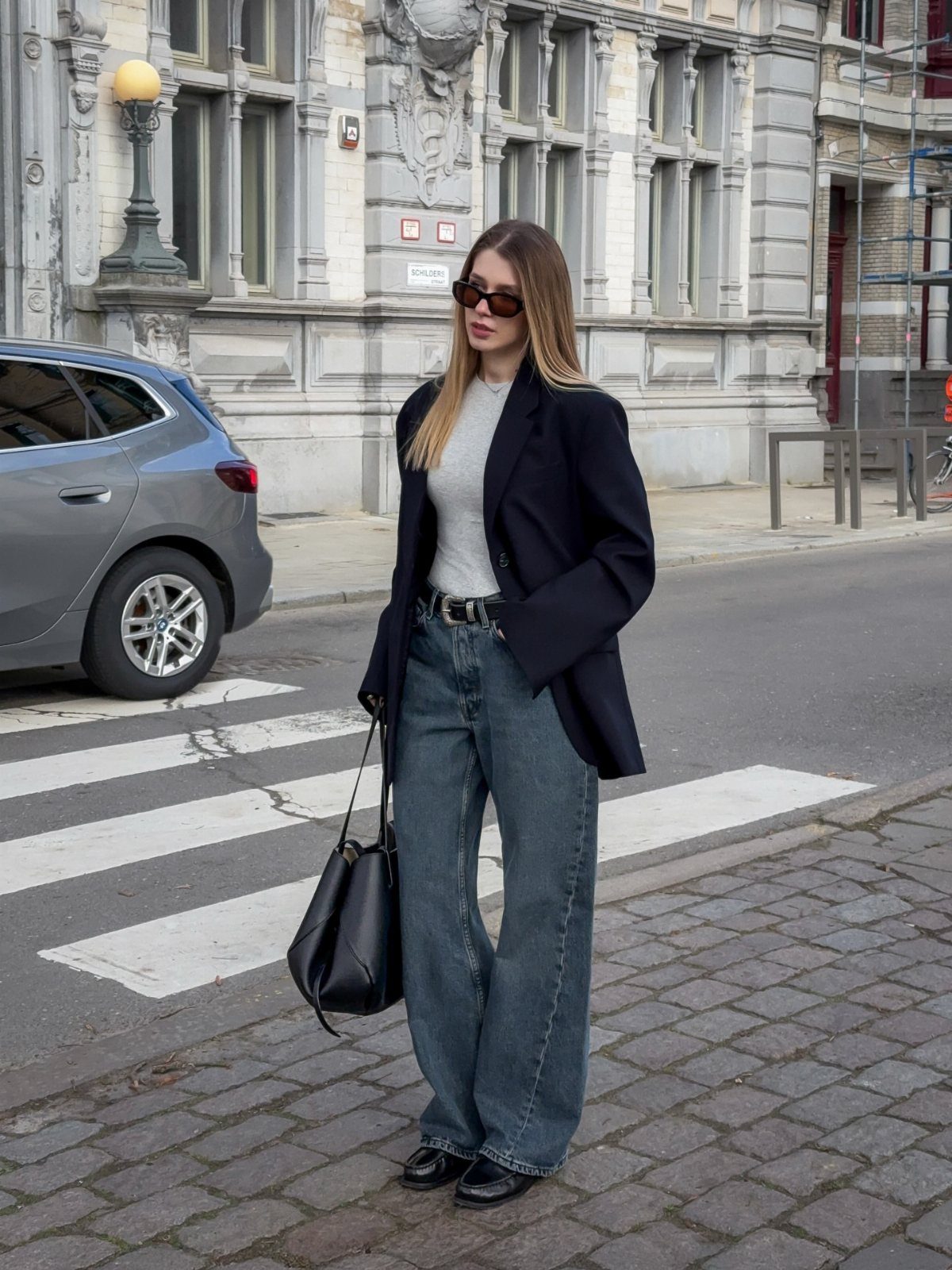 11 Casual Travel Outfit Ideas for Women (2026) 4 Woman wearing a navy blazer and wide-leg blue jeans on a city street.
