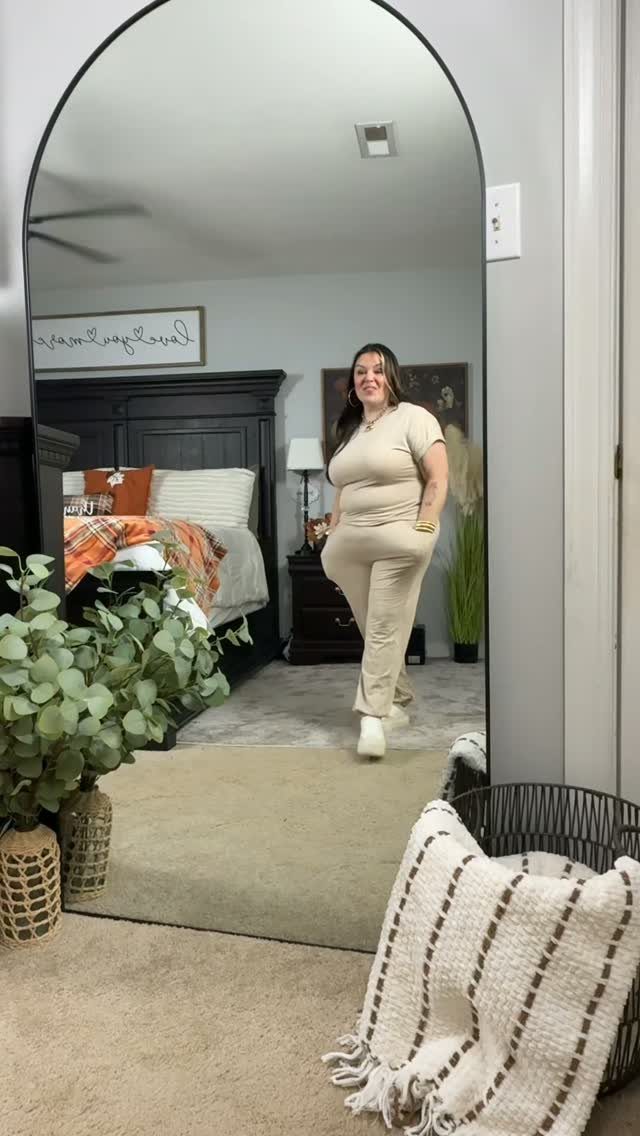 11 Casual Travel Outfit Ideas for Women (2026) 1 Woman wearing a matching beige lounge set and white sneakers in a bedroom mirror.