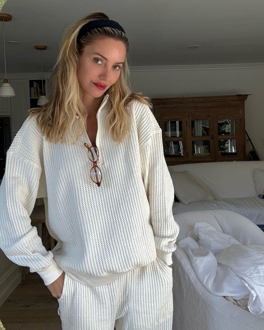 11 Casual Travel Outfit Ideas for Women (2026) 8 Woman wearing a white waffle-knit matching pullover and pants set in a bedroom.