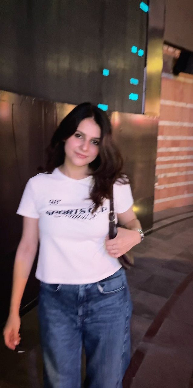 11 Casual Travel Outfit Ideas for Women (2026) 9 Woman wearing a white graphic t-shirt and blue jeans in an indoor setting.