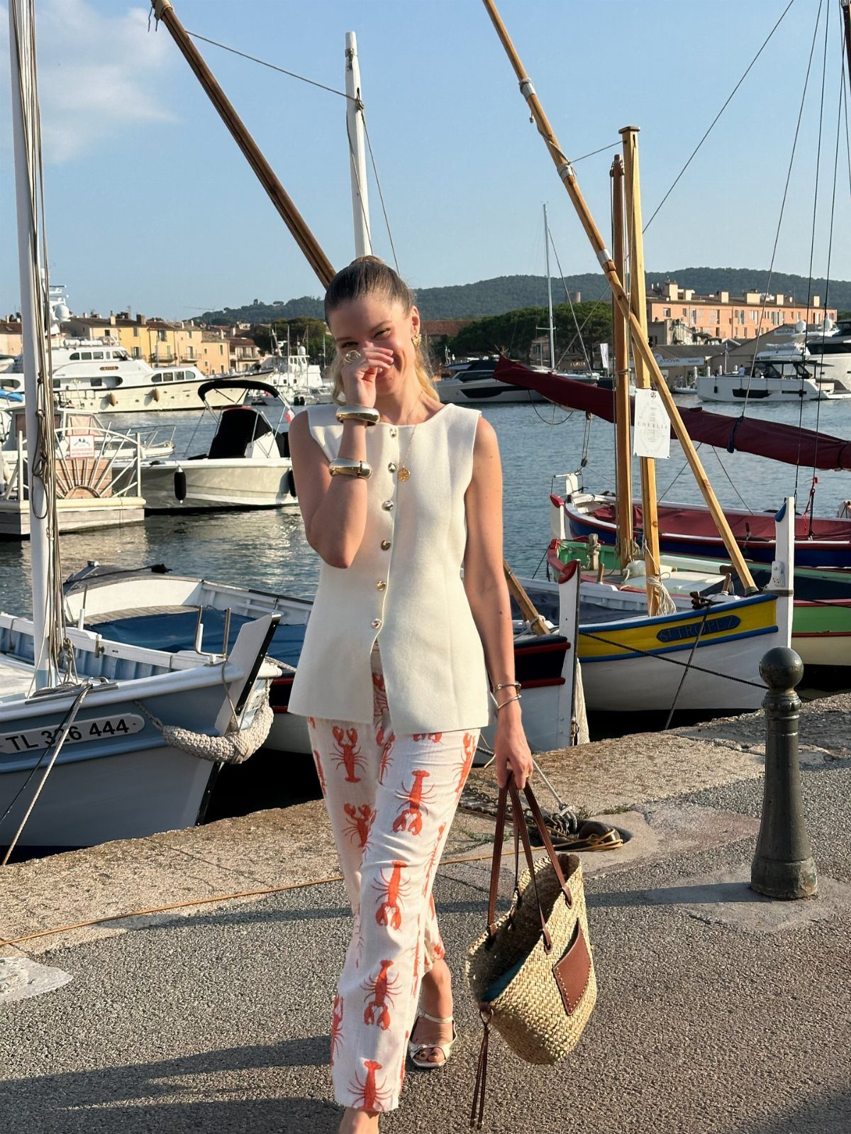 10 Chic Summer Outfits: Sandals, Linen, Dresses and More 10 Woman in a white vest and lobster print trousers walking by a harbor with boats.