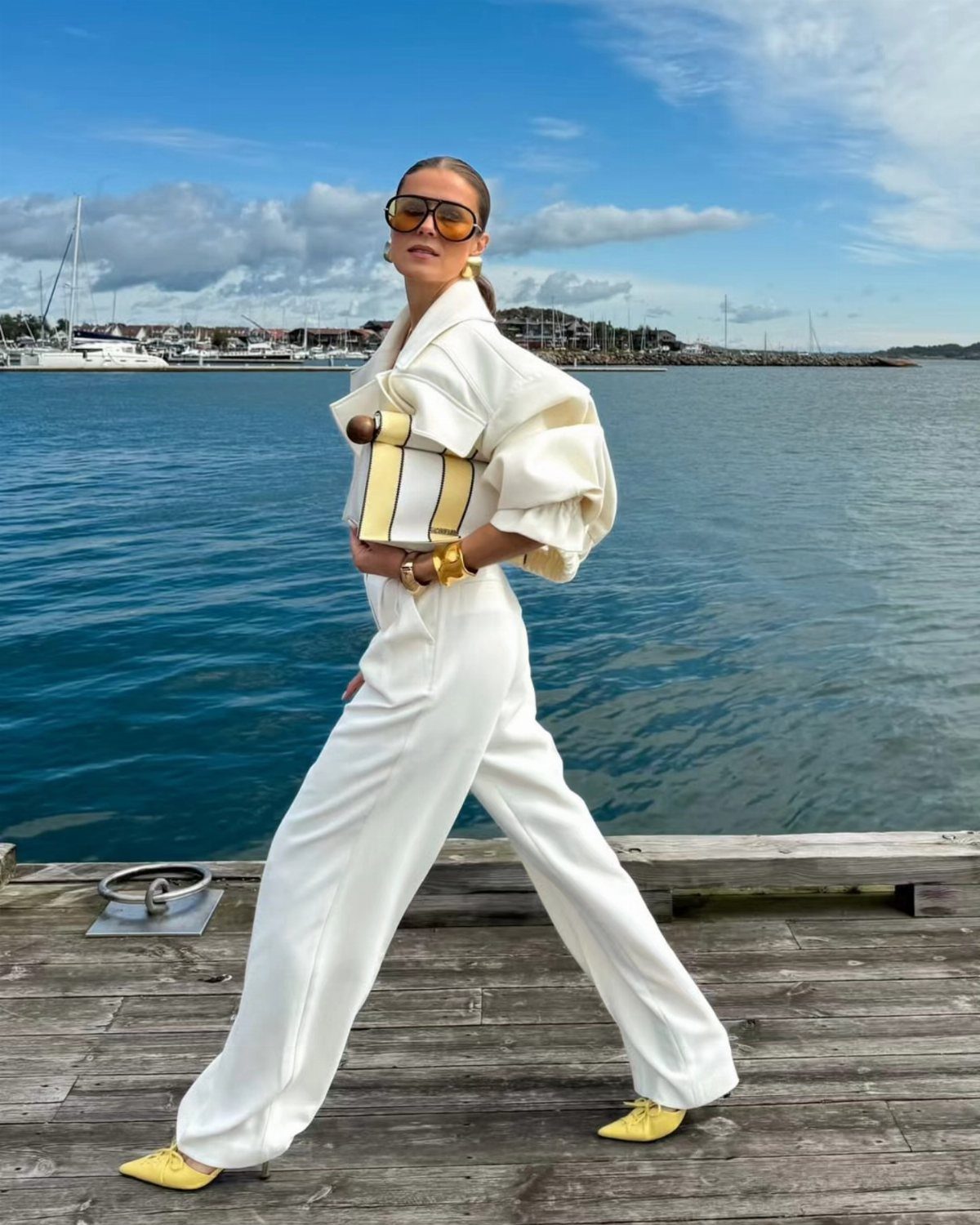 10 Chic Summer Outfits: Sandals, Linen, Dresses and More 9 Woman in a white structured blazer and trousers posing on a pier by the sea.