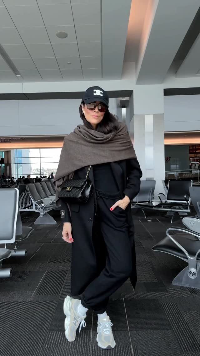 Chic Travel Outfits for Women: 14 Stylish Ideas for 2026 13 Woman in black airport attire with a brown shawl and white sneakers.