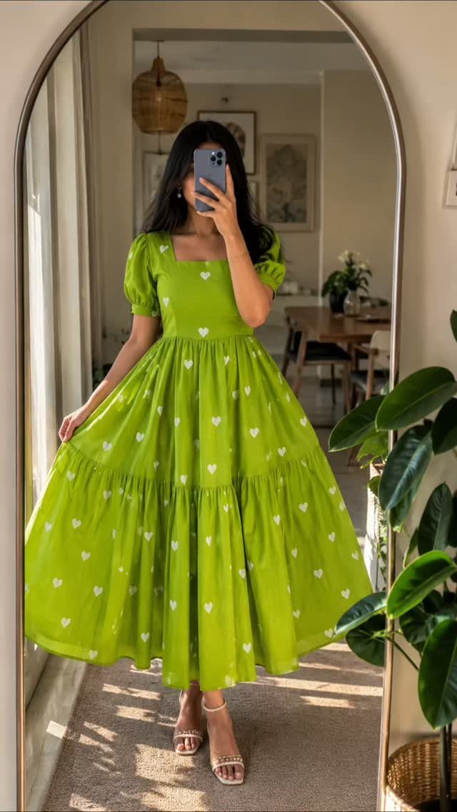 Chic Travel Outfits for Women: 14 Stylish Ideas for 2026 1 Woman in a lime green heart-print maxi dress and white sandals taking a selfie.
