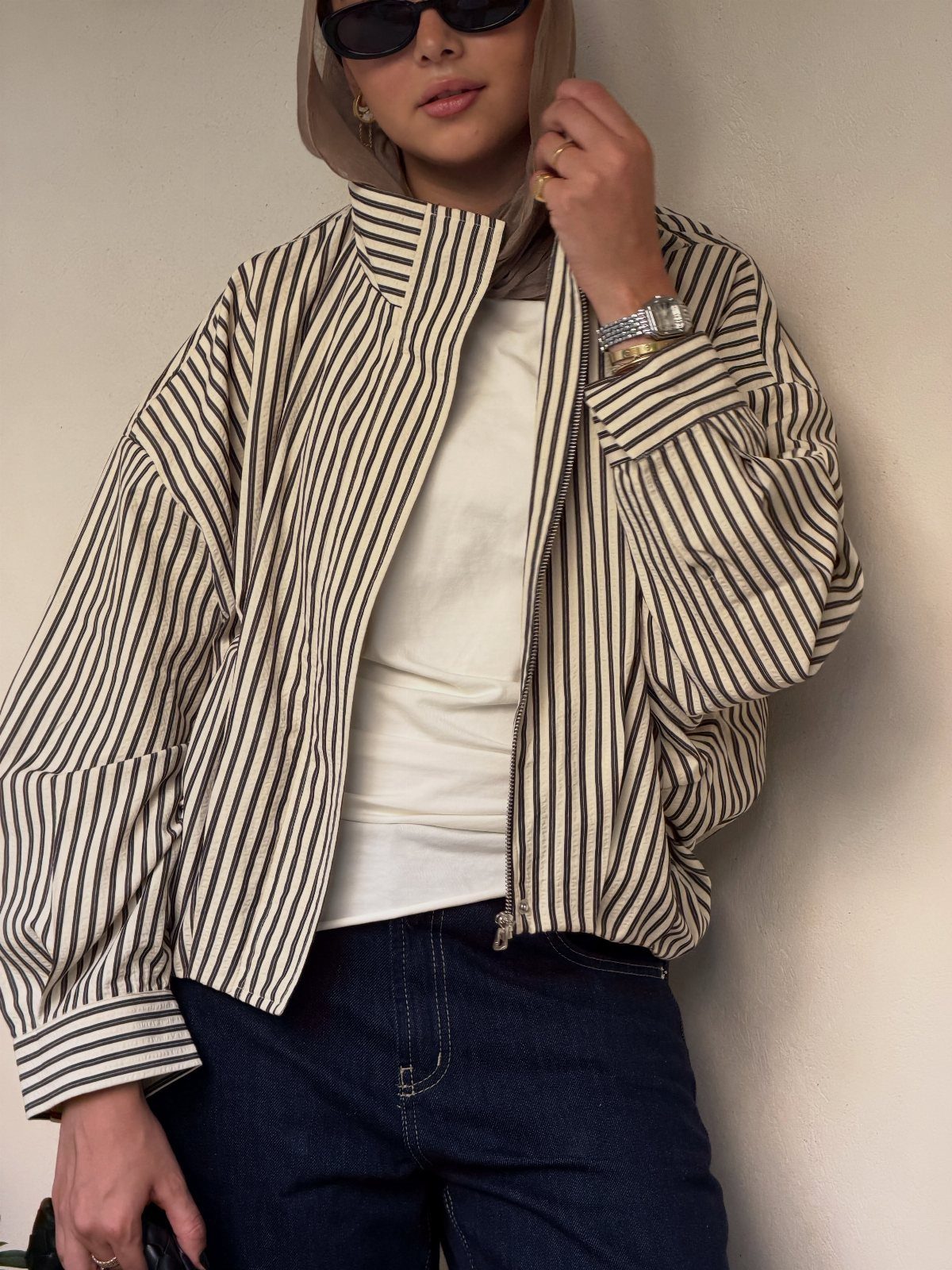 Chic Travel Outfits for Women: 14 Stylish Ideas for 2026 11 Woman in a striped cream jacket, white top, and dark blue jeans wearing sunglasses.