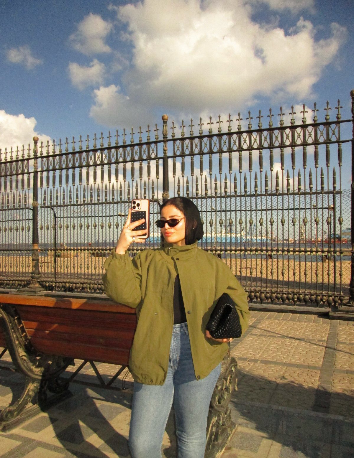Chic Travel Outfits for Women: 14 Stylish Ideas for 2026 12 Woman in olive green utility jacket and blue jeans posing by a black fence.