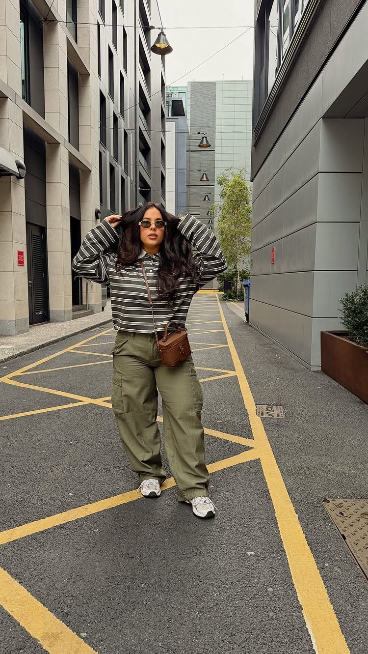 Chic Travel Outfits for Women: 14 Stylish Ideas for 2026 6 Woman wearing olive green utility pants and a striped shirt in a city alley.