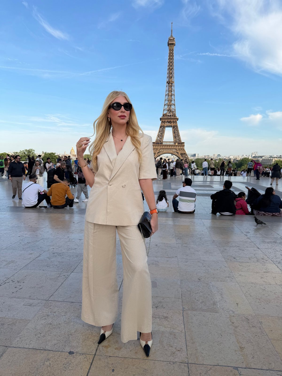 Chic Travel Outfits for Women: 14 Stylish Ideas for 2026 3 Woman in cream blazer and wide-leg trousers posing before the Eiffel Tower in Paris.