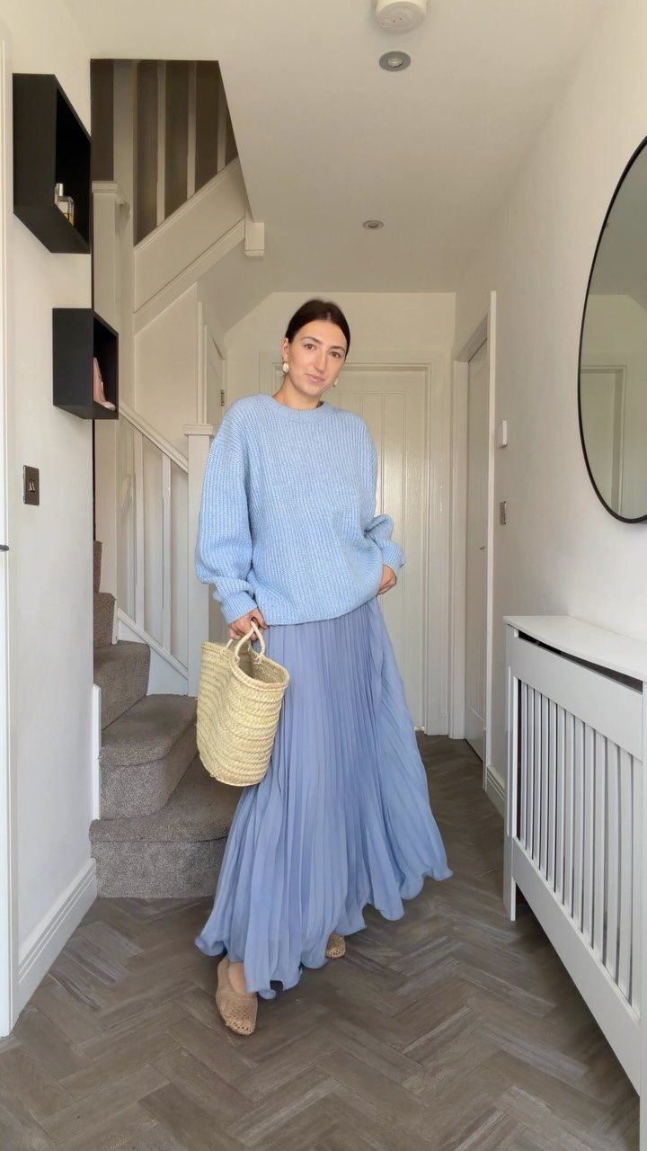 26 Classy Date Outfits From Casual to Elegant 9 Woman wearing a light blue sweater and pleated maxi skirt in a hallway.