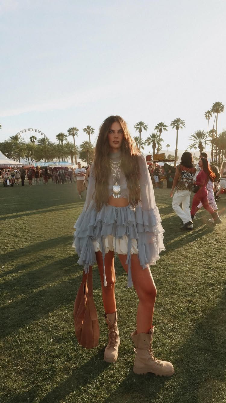 Coachella Outfits for Women: 14 Festival Looks That Work 1 Woman in a ruffled sheer blue top and combat boots standing on a grassy festival field.