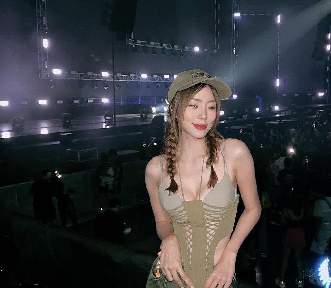 Coachella Outfits for Women: 14 Festival Looks That Work 4 A smiling woman with braids wearing a tan corset top and a khaki cap at a concert.