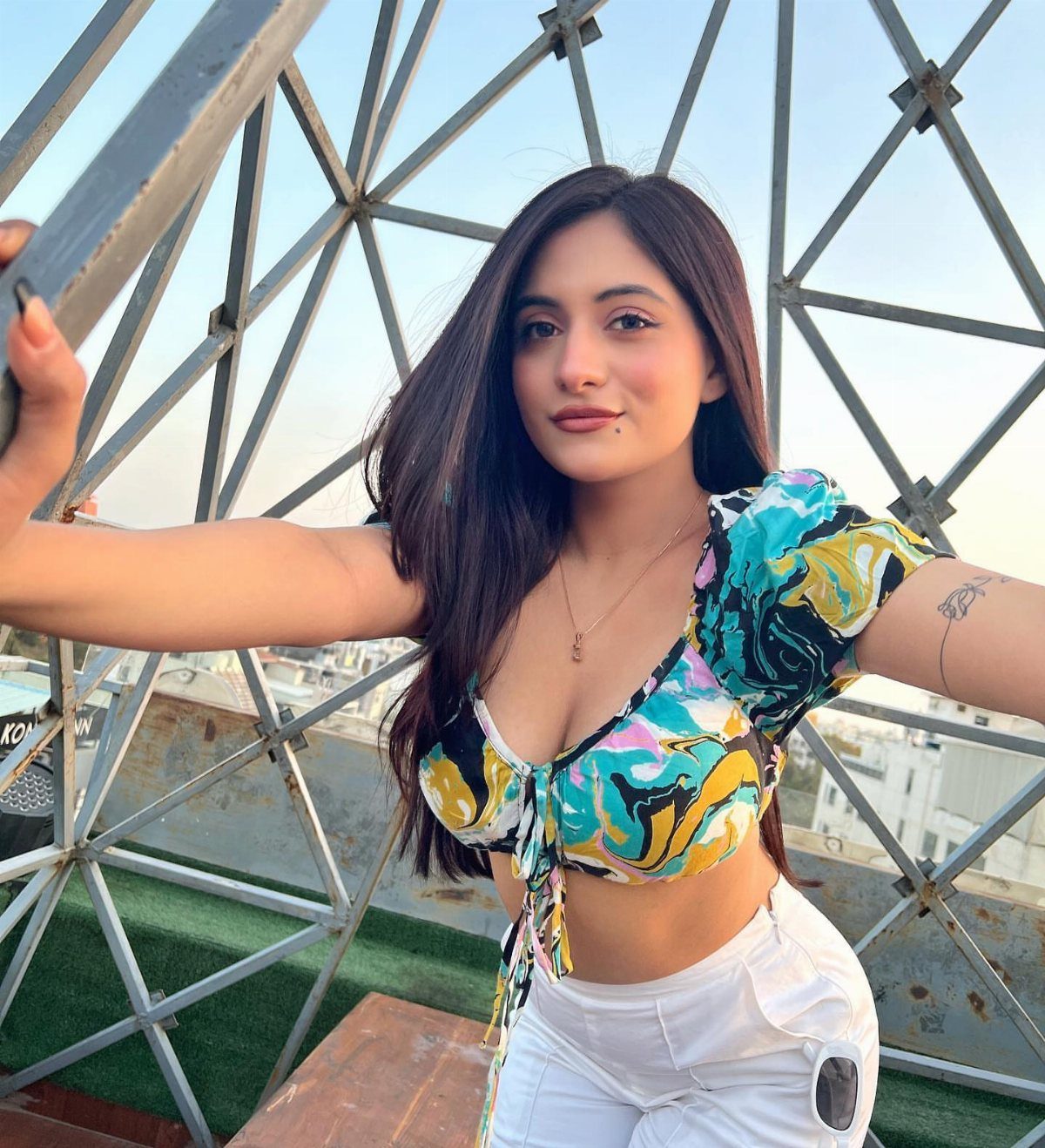 Woman wearing a colorful patterned crop top and white pants posing by metal beams.