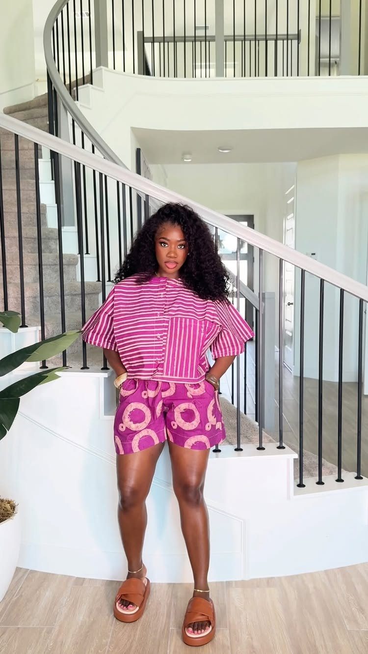 Woman wearing a striped pink shirt, patterned pink shorts, and brown slide sandals.