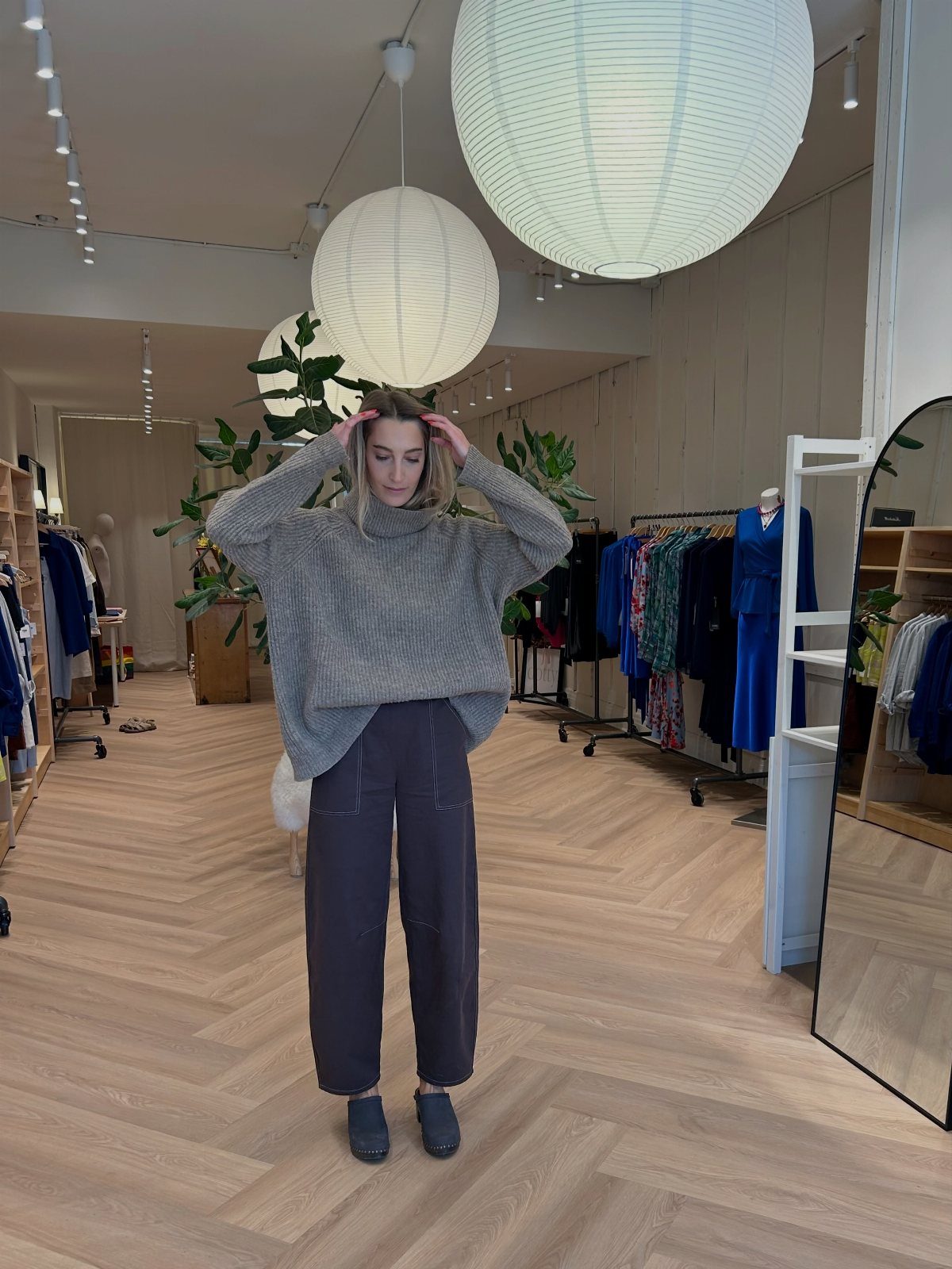 Woman wearing an oversized grey knit sweater and dark grey barrel-shaped trousers.