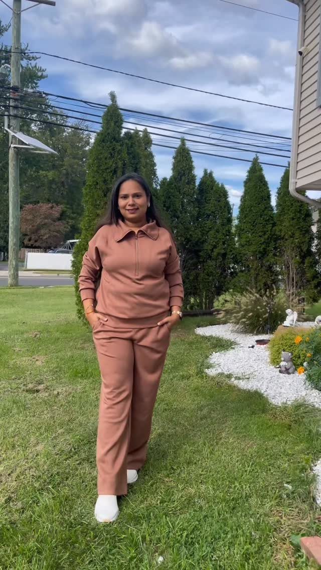 Woman in brown quarter-zip pullover and matching trousers standing on a green lawn.