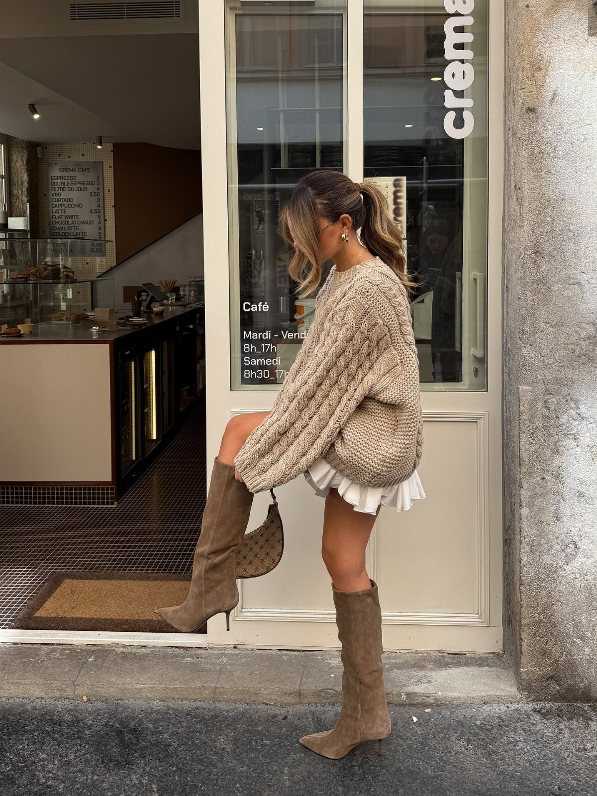 Woman in oversized beige cable-knit sweater, white mini skirt, and brown suede boots.