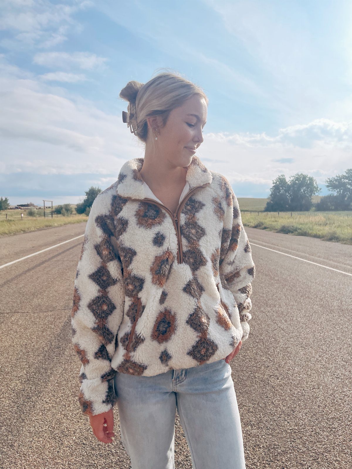 Woman wearing a patterned fuzzy quarter-zip pullover and light blue jeans on a road.