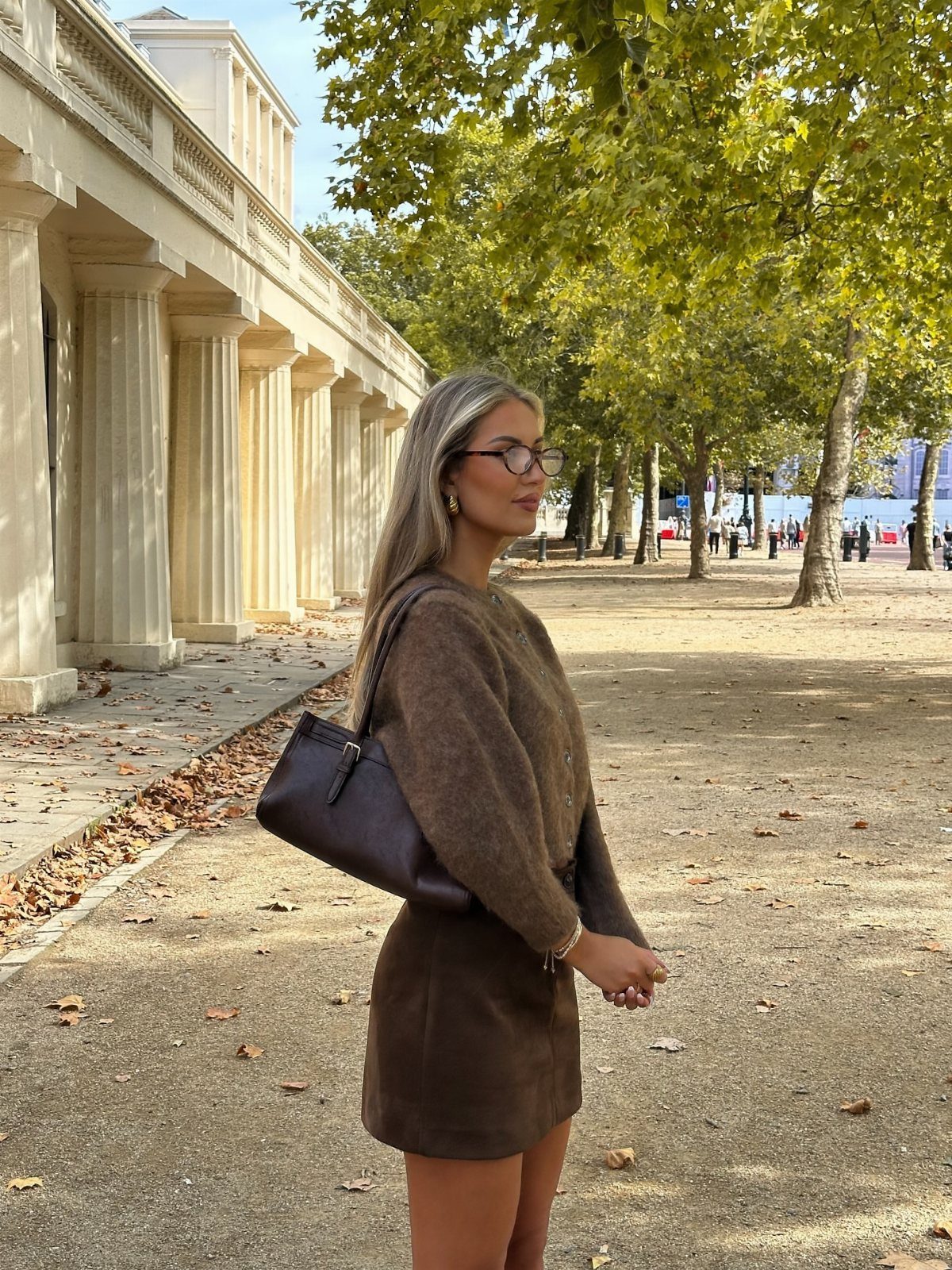 Woman wearing a brown knit sweater and short suede skirt in an autumn setting.