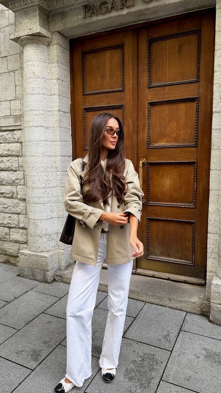 Woman wearing a beige utility jacket and white wide-leg trousers by a wooden door.