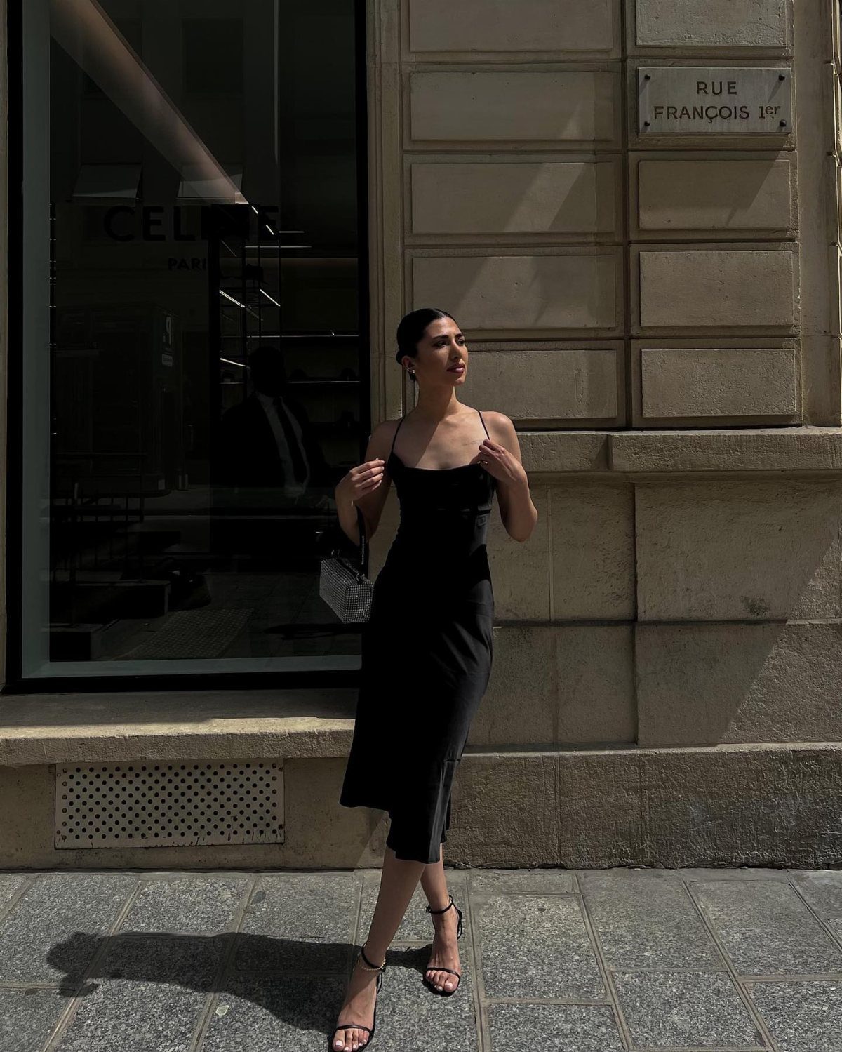 Woman wearing a black midi slip dress and strappy heels on a city street.