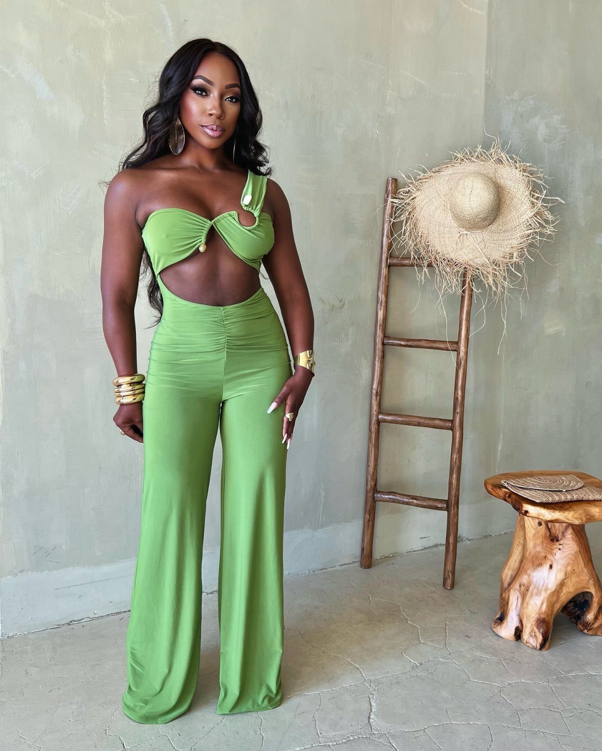 Woman wearing a lime green one-shoulder cutout jumpsuit standing in a neutral room.