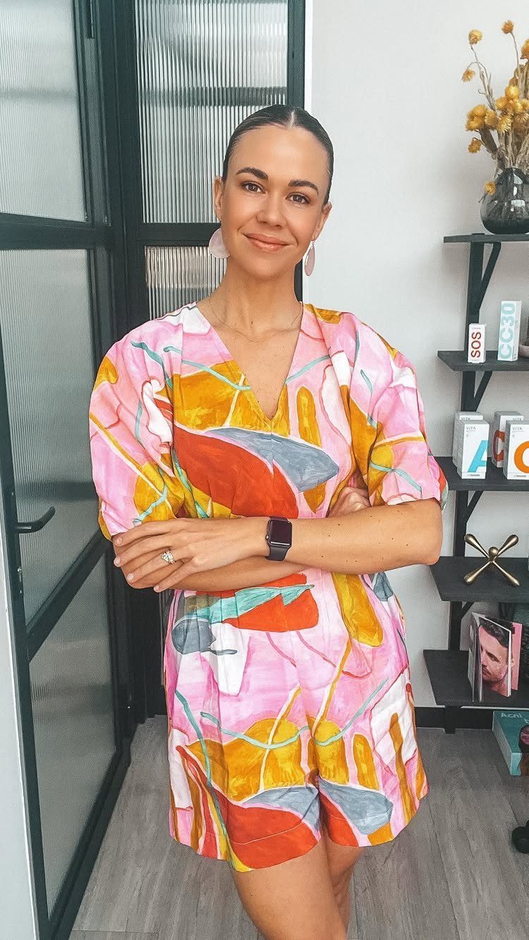 A smiling woman posing in a colorful pink and orange patterned summer romper.