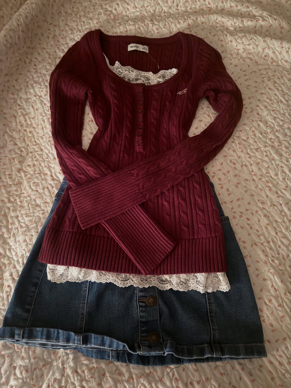 Maroon cable-knit lace-trimmed sweater and a denim skirt laid flat on a cream textured surface.