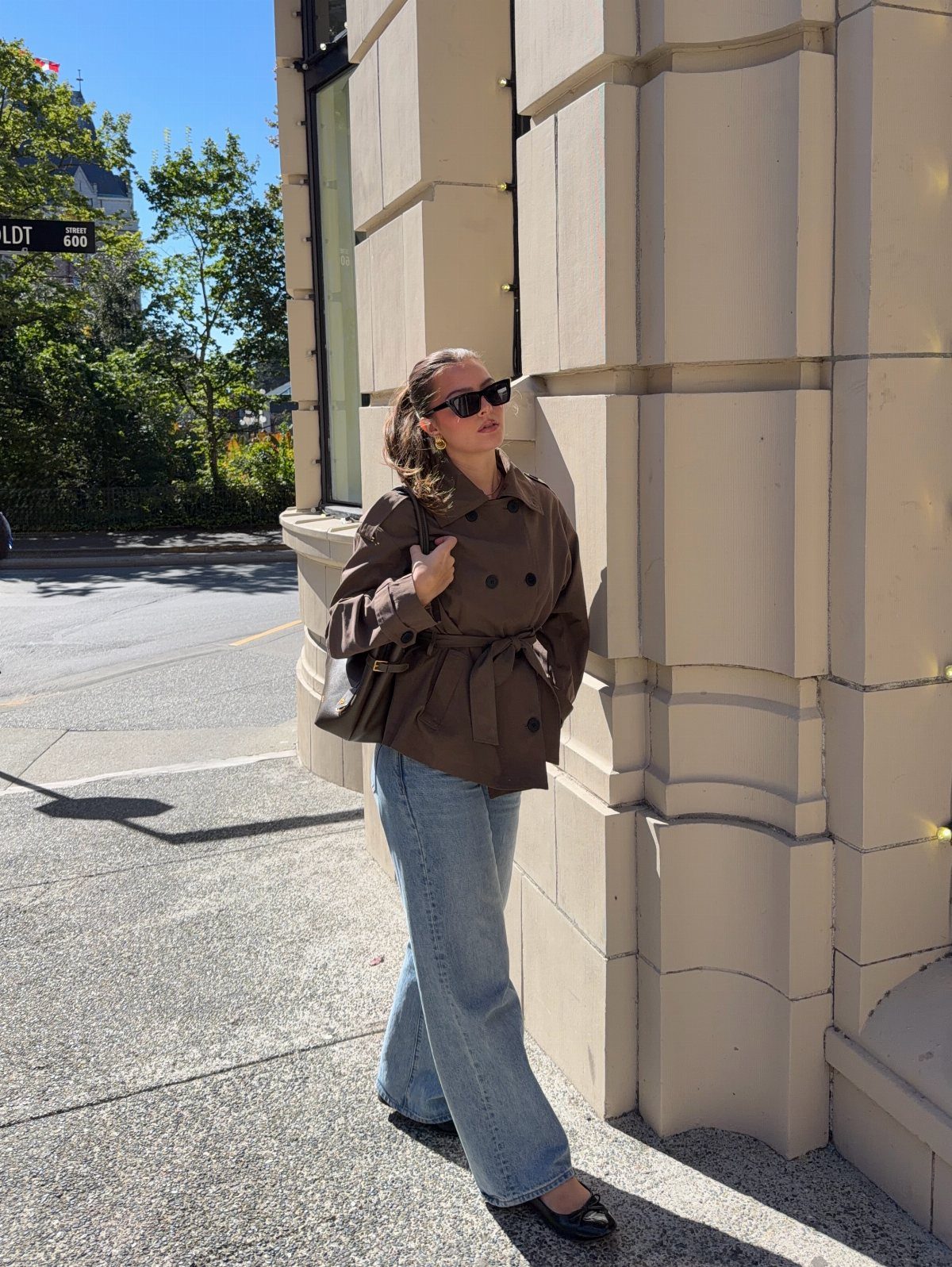 Woman walking in light blue wide-leg jeans and a brown belted trench coat.