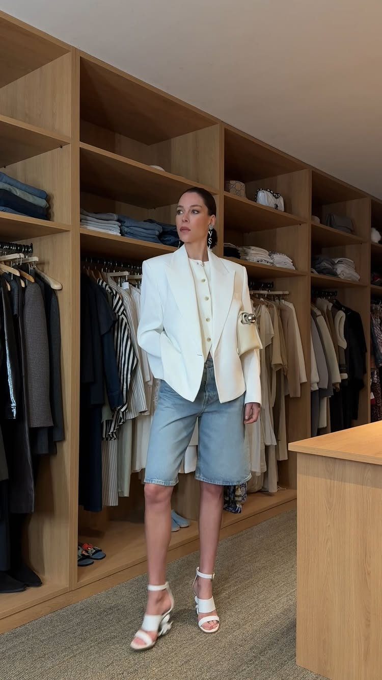 Woman wearing a white blazer and light blue denim shorts in a closet.