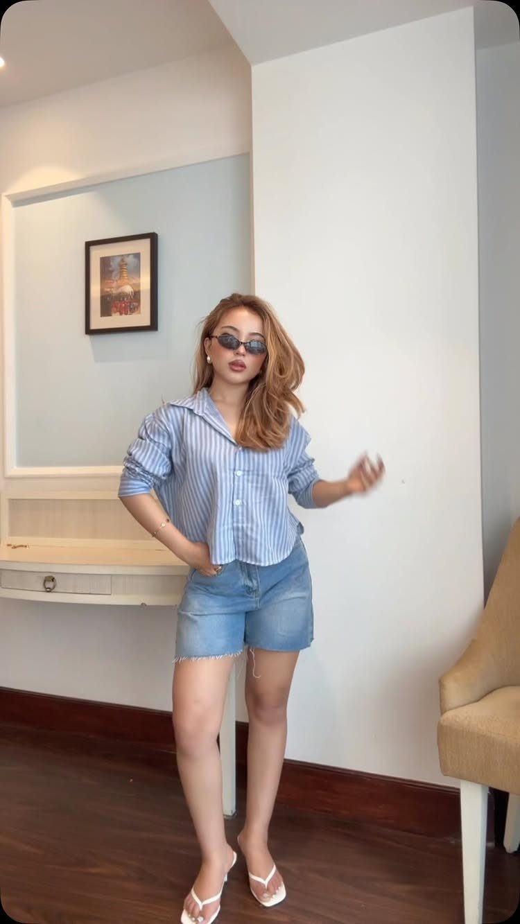 Woman wearing a blue striped shirt and denim shorts with white flip-flops.