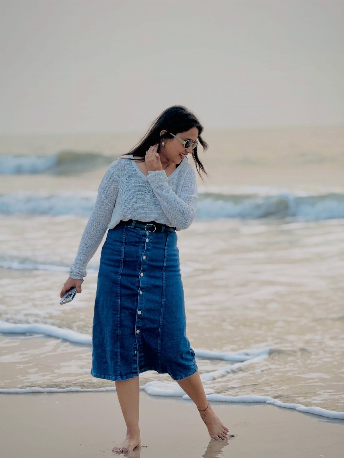 Denim Skirt Outfits: 19 Ways to Style Them This Season 14 Woman in a blue denim midi skirt and light top standing on a beach.