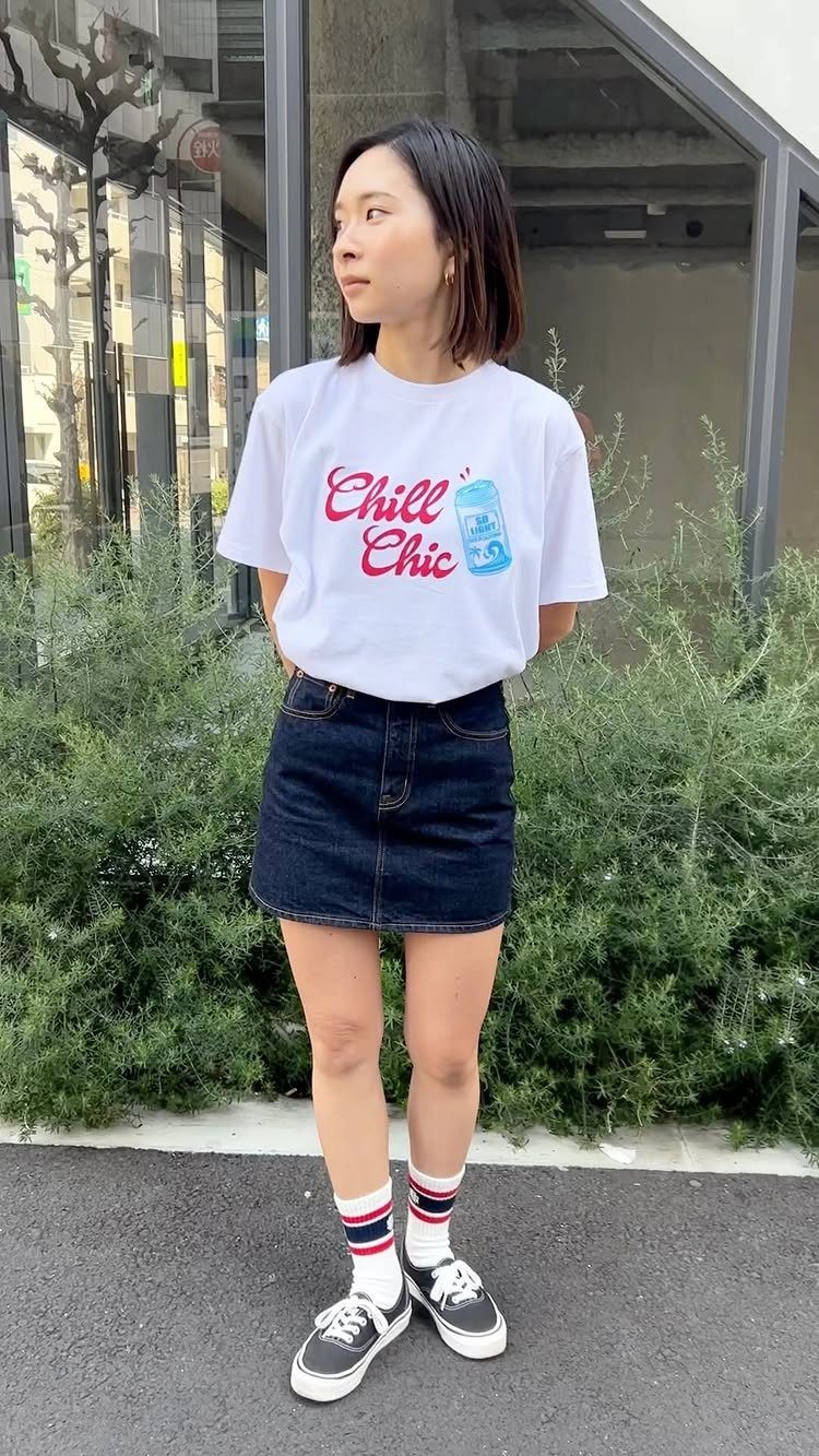 Denim Skirt Outfits: 19 Ways to Style Them This Season 5 Woman wearing a white graphic tee and dark blue denim mini skirt with sneakers.