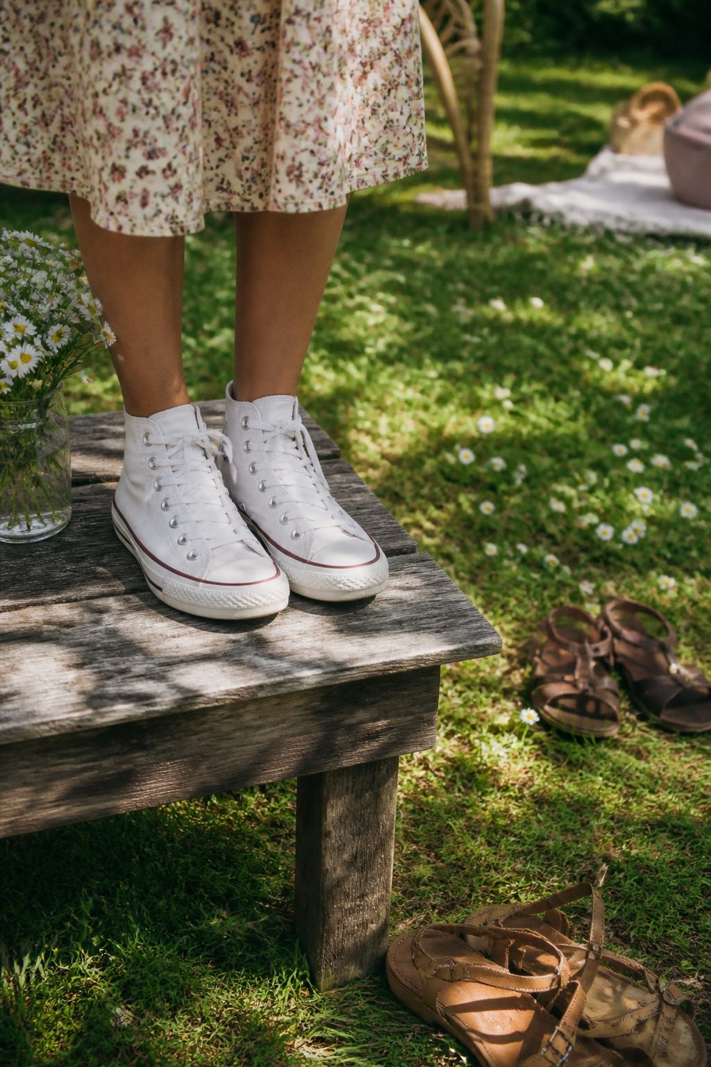 Converse sneakers on a wooden bench next to a floral dress.