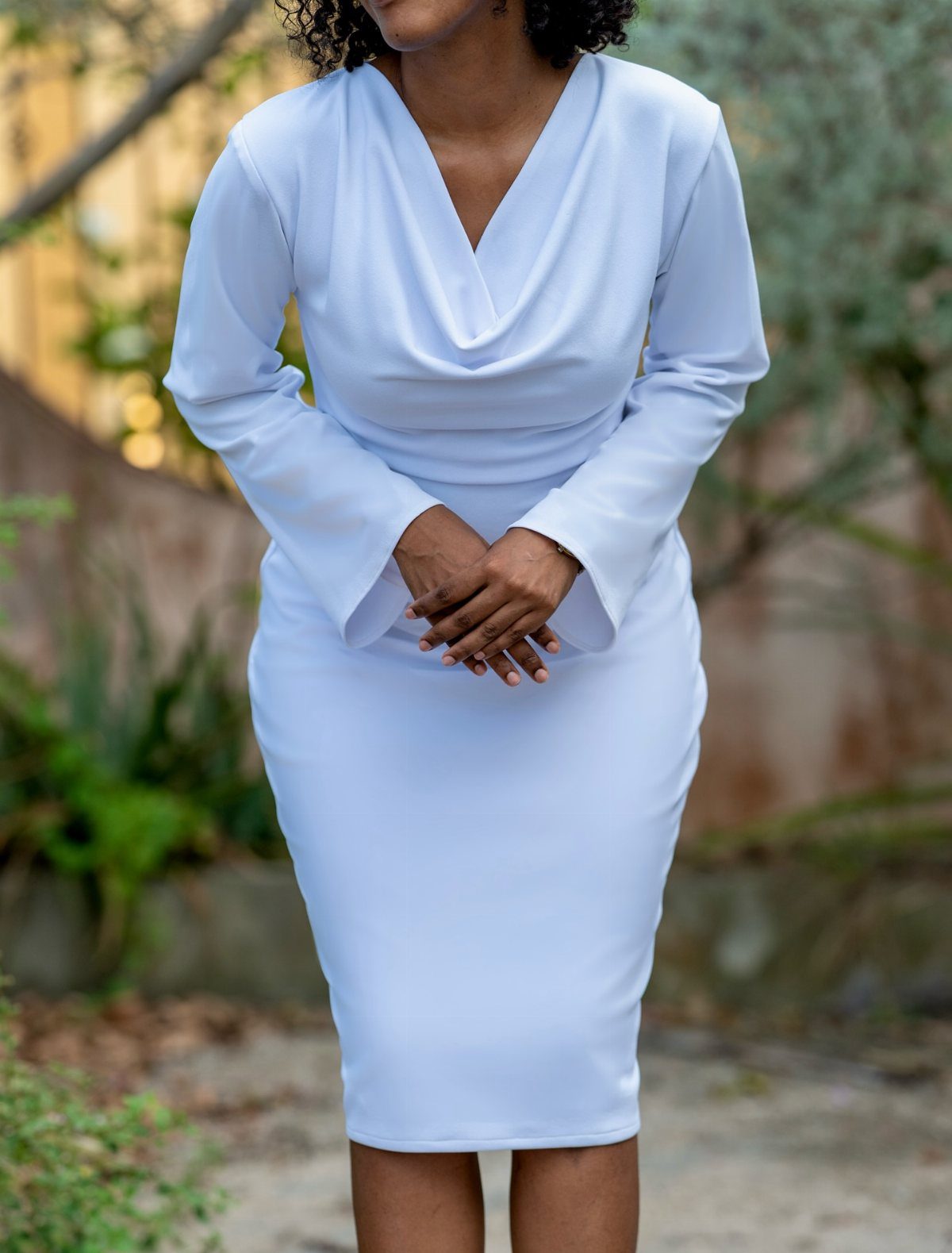 Woman wearing a white long-sleeved midi dress with a cowl neckline outdoors.