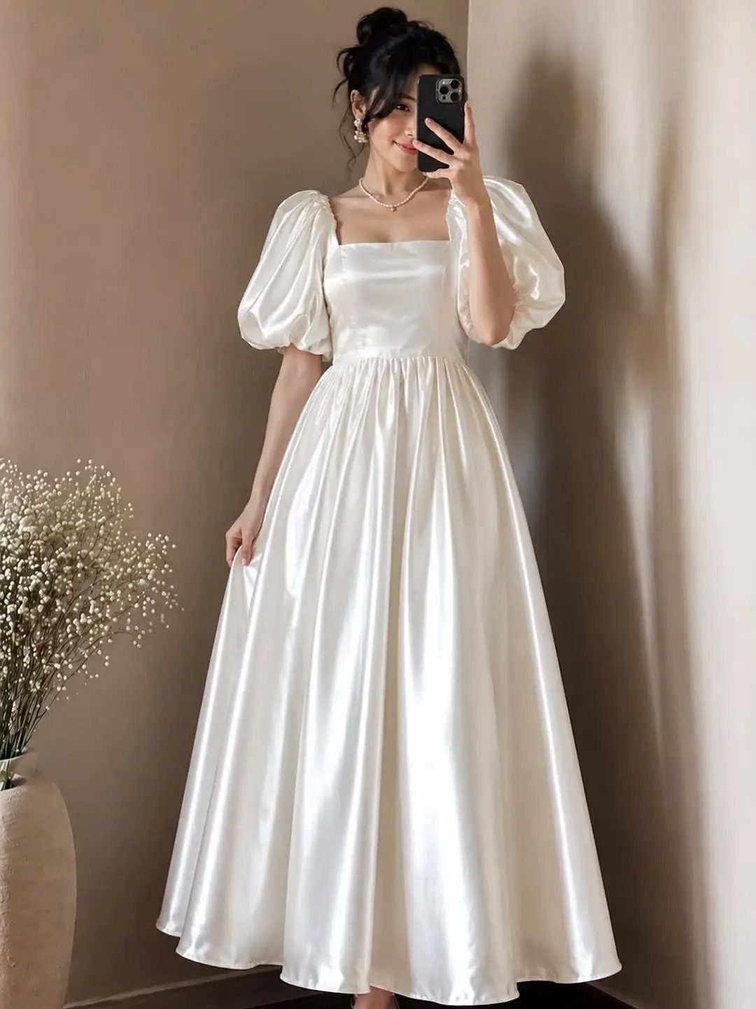 Woman in a white satin puff sleeve maxi dress taking a mirror selfie.