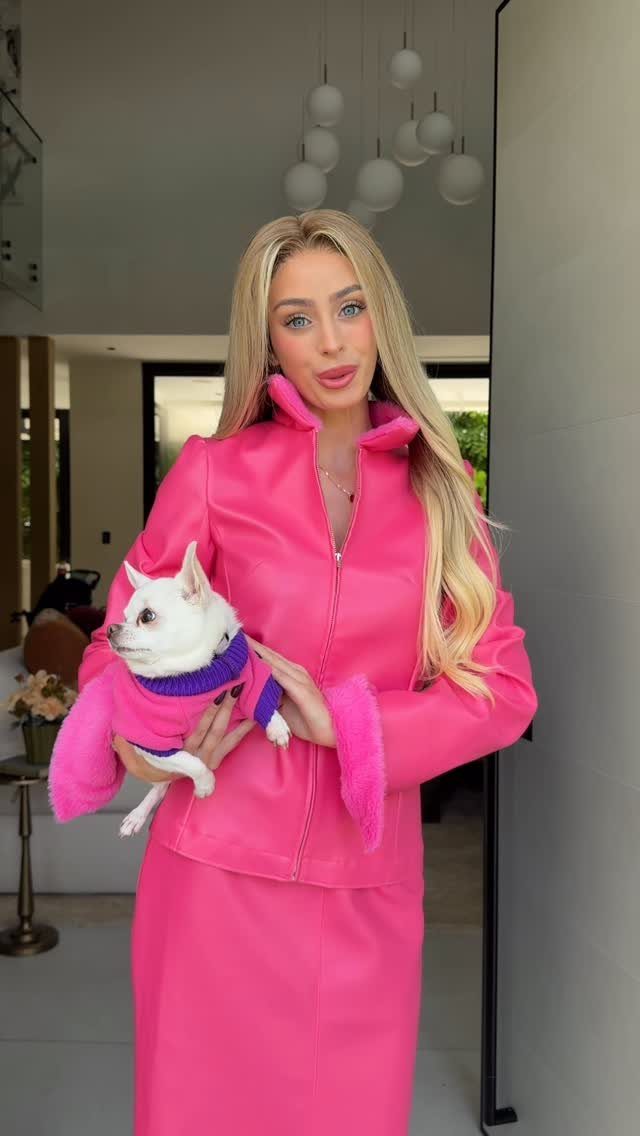 Blonde woman in a bright pink leather outfit holding a small white chihuahua.