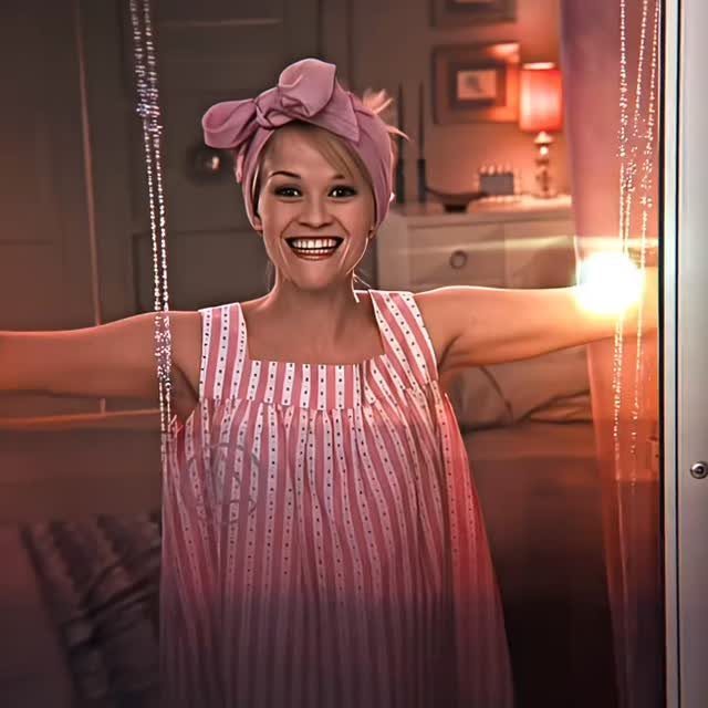 A smiling blonde woman wearing a pink bow headband and a pink striped dress.