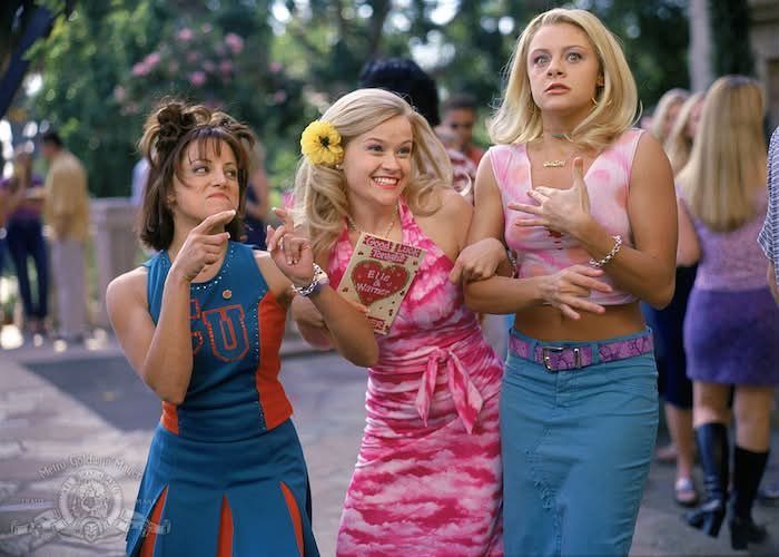 Three women walking outdoors wearing colorful pink, blue, and orange fashionable outfits.