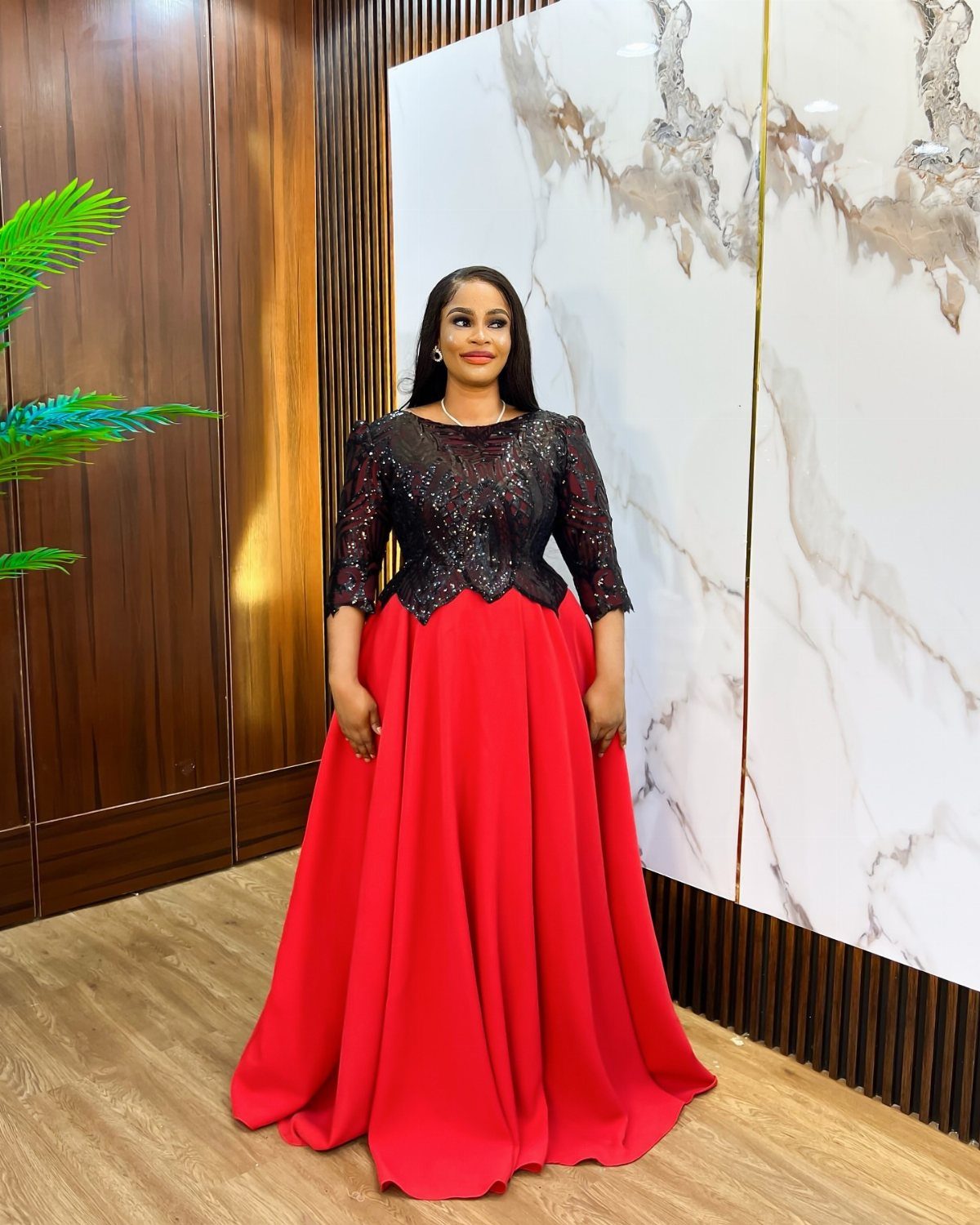 Woman in a red maxi gown with a black embellished empire waist bodice.