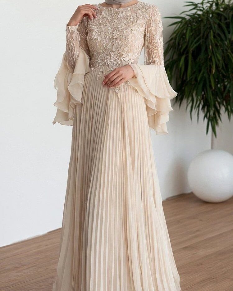 Woman in a champagne lace and pleated evening gown with ruffled sleeves.
