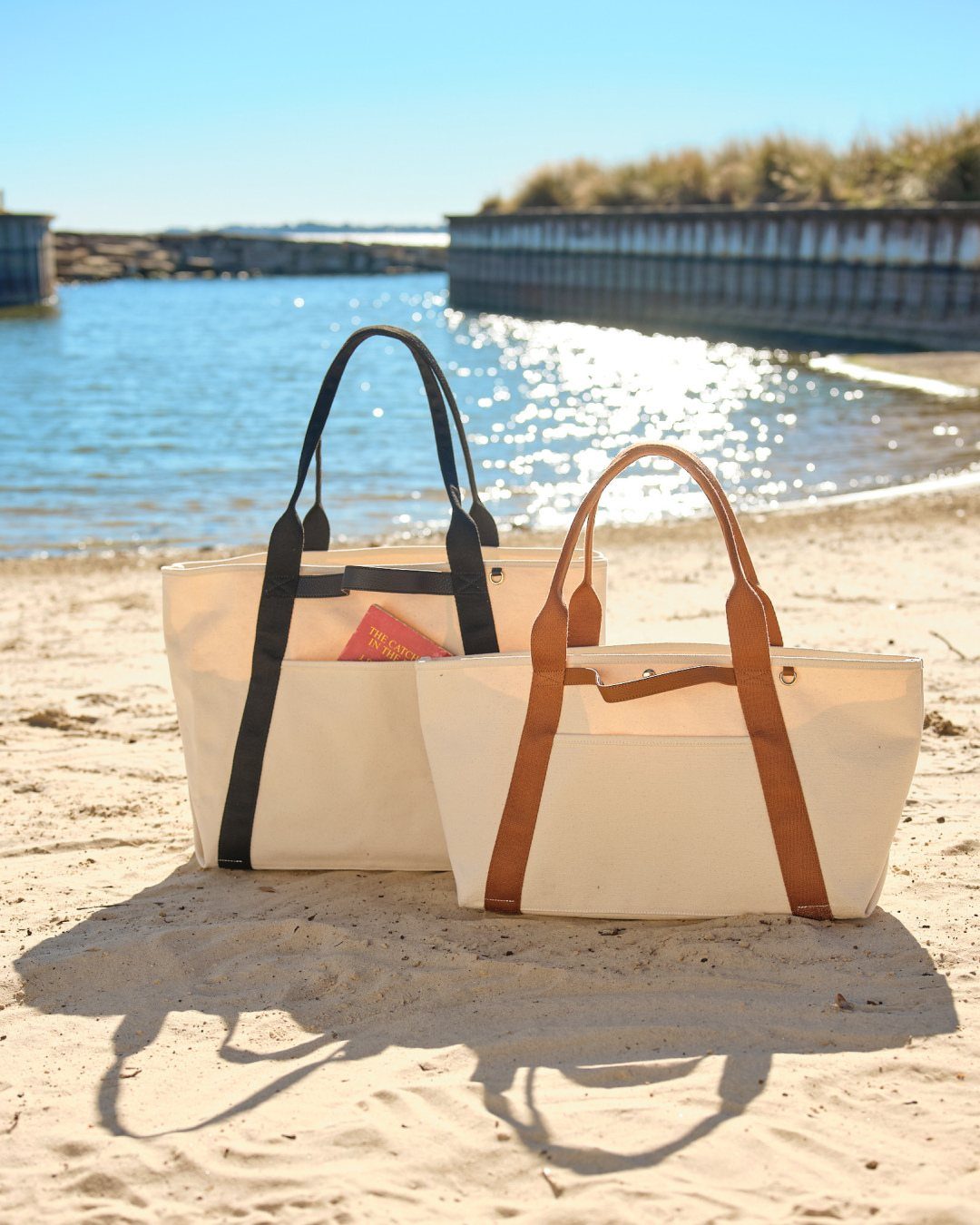 Fall Beach Outfits: 20 Ideas for Your Coastal Getaway 11 Two cream canvas tote bags with black and brown straps on a sandy beach.
