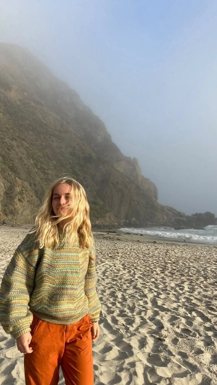 Fall Beach Outfits: 20 Ideas for Your Coastal Getaway 18 Woman wearing a knit sweater and orange pants on a foggy beach.
