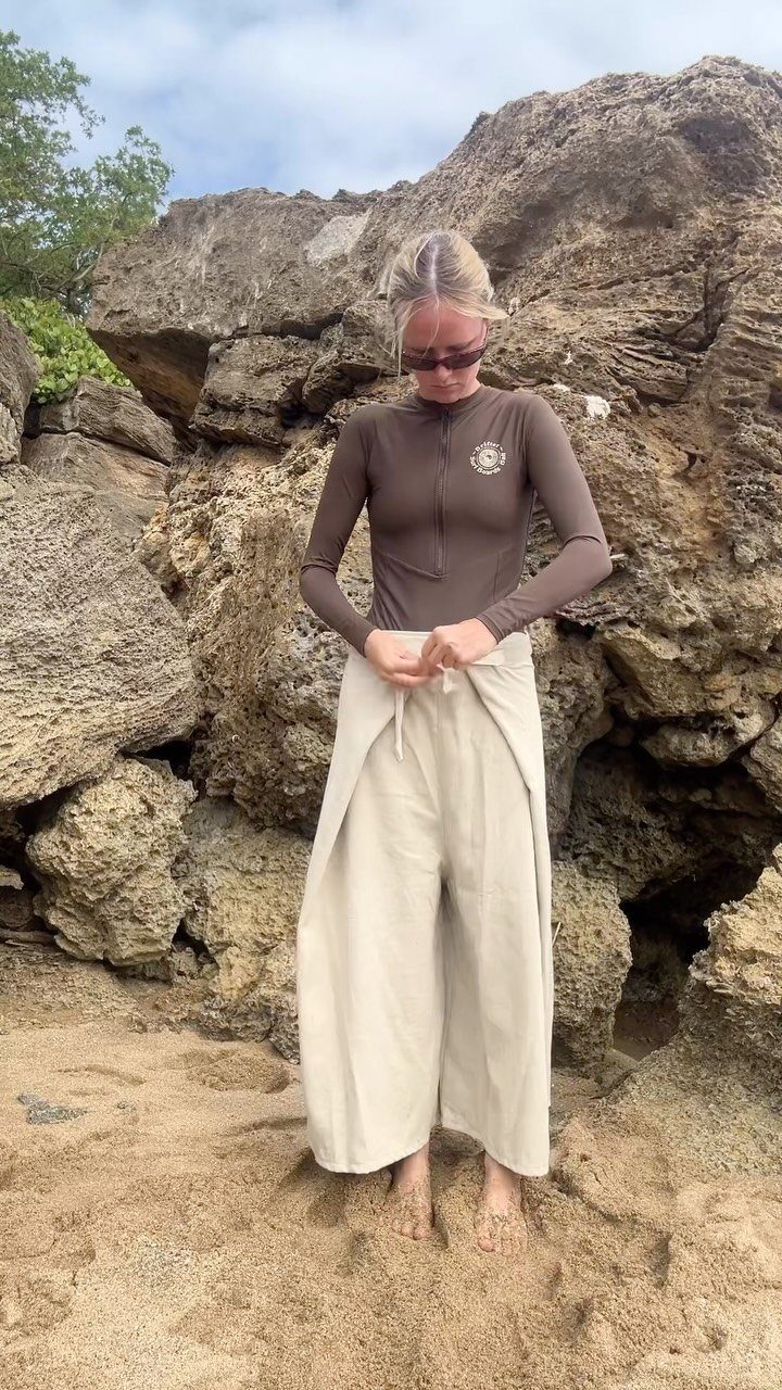 Fall Beach Outfits: 20 Ideas for Your Coastal Getaway 8 Woman on a sandy beach wearing a brown top and wide-leg flowing cream pants.