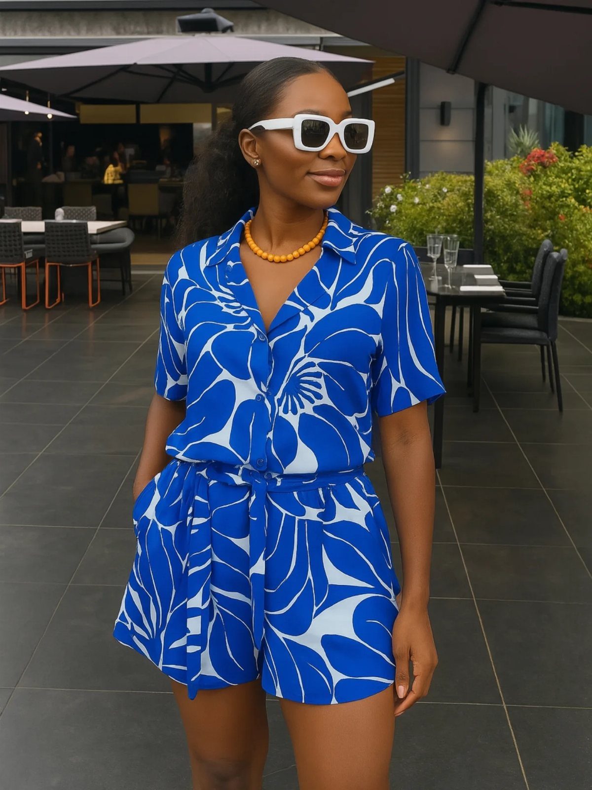 Fall Beach Outfits: 20 Ideas for Your Coastal Getaway 1 Woman wearing a blue and white floral print romper and white sunglasses outdoors.