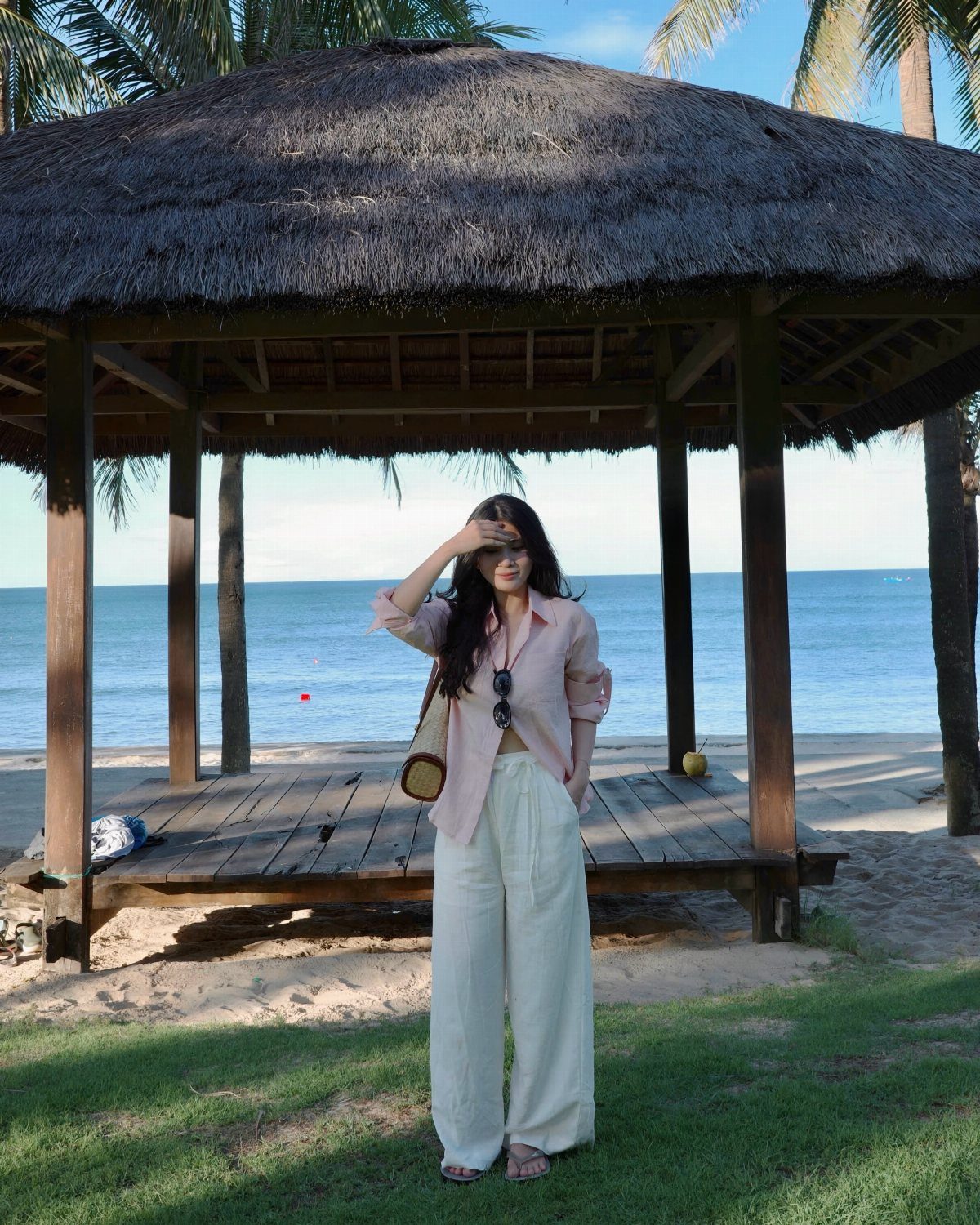 Fall Beach Outfits: 20 Ideas for Your Coastal Getaway 3 Woman wearing a pink shirt and white wide-leg linen pants on a beach.