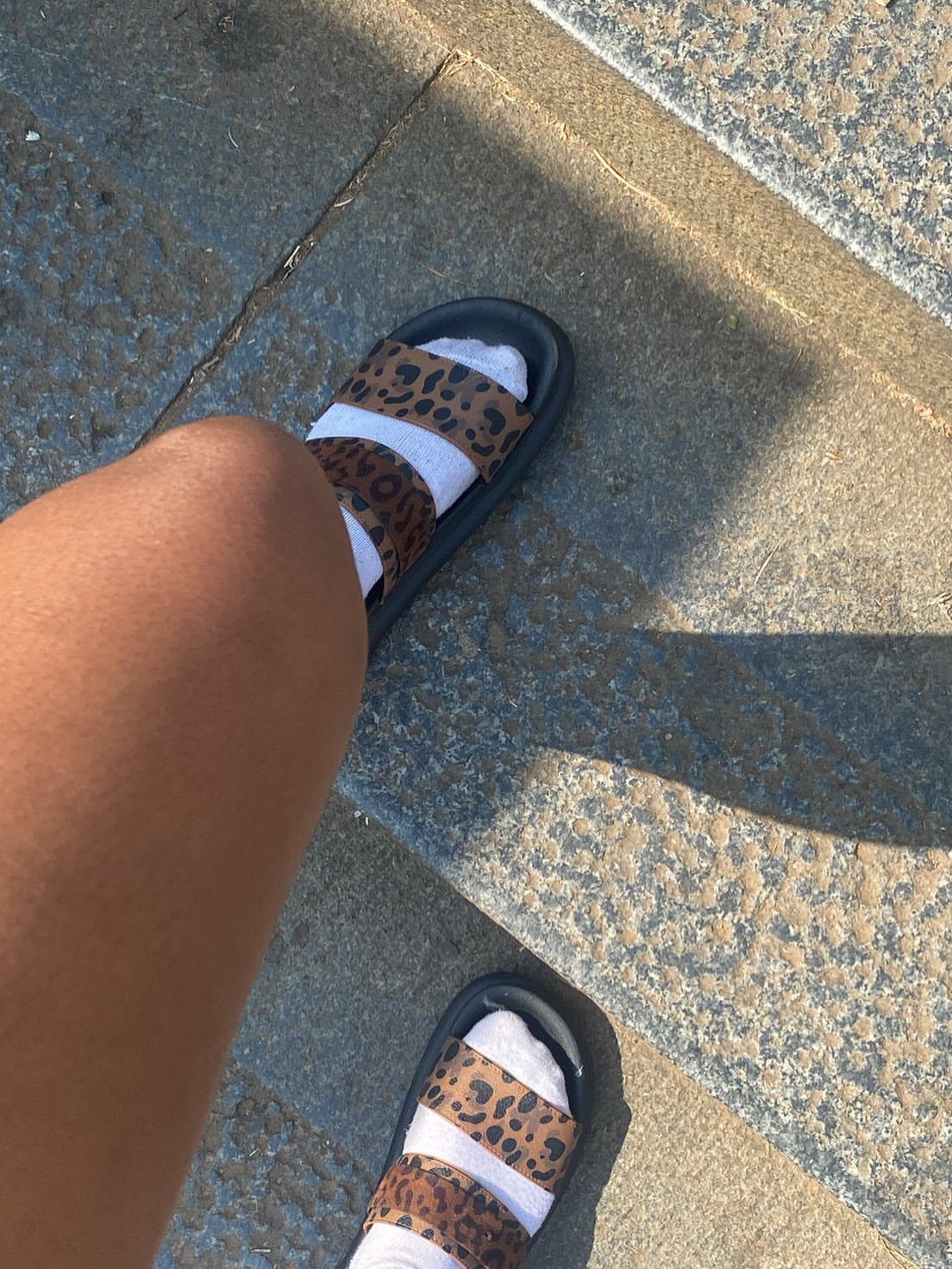Fall Beach Outfits: 20 Ideas for Your Coastal Getaway 16 Leopard-print slide sandals worn over white socks on a grey stone surface.