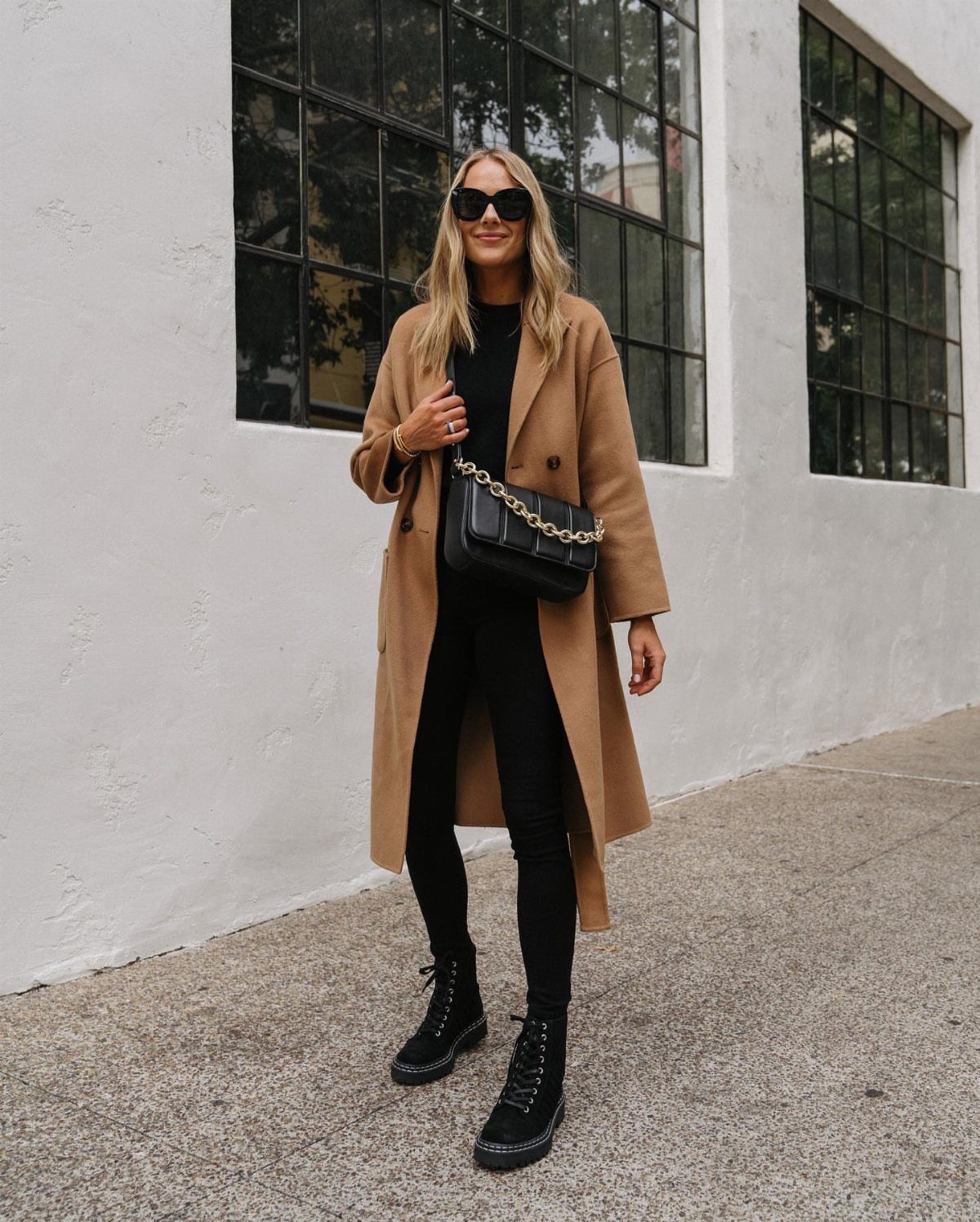 Woman in tan trench coat, black trousers, and black combat boots standing outdoors.