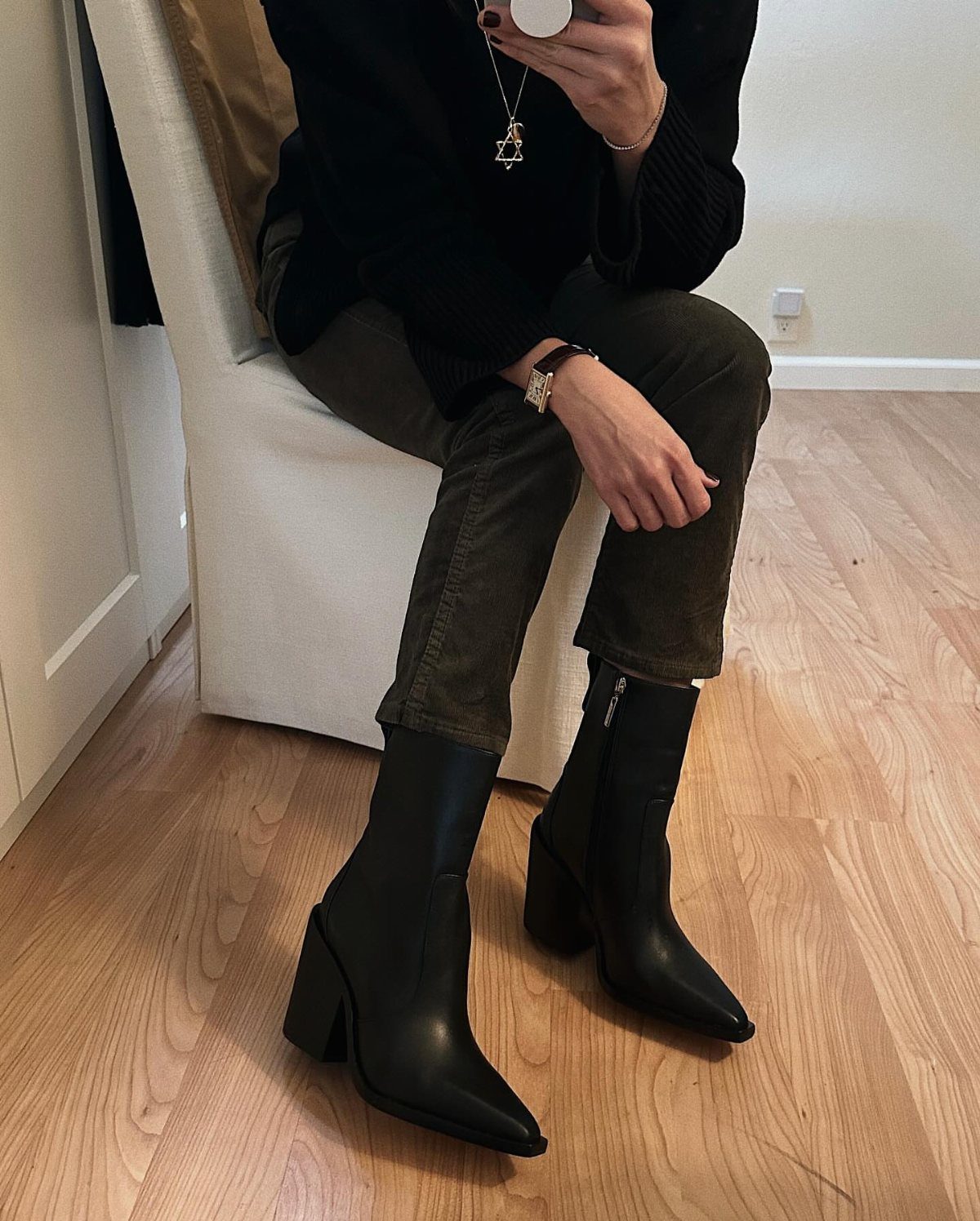 Olive green corduroy trousers paired with black pointed-toe ankle boots and a black top.